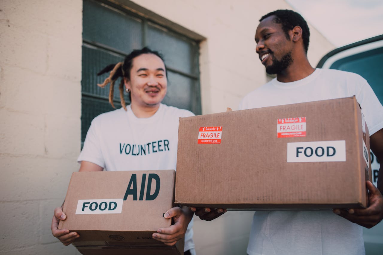 About Two volunteers carrying aid boxes labeled food, showing community support and charity efforts.