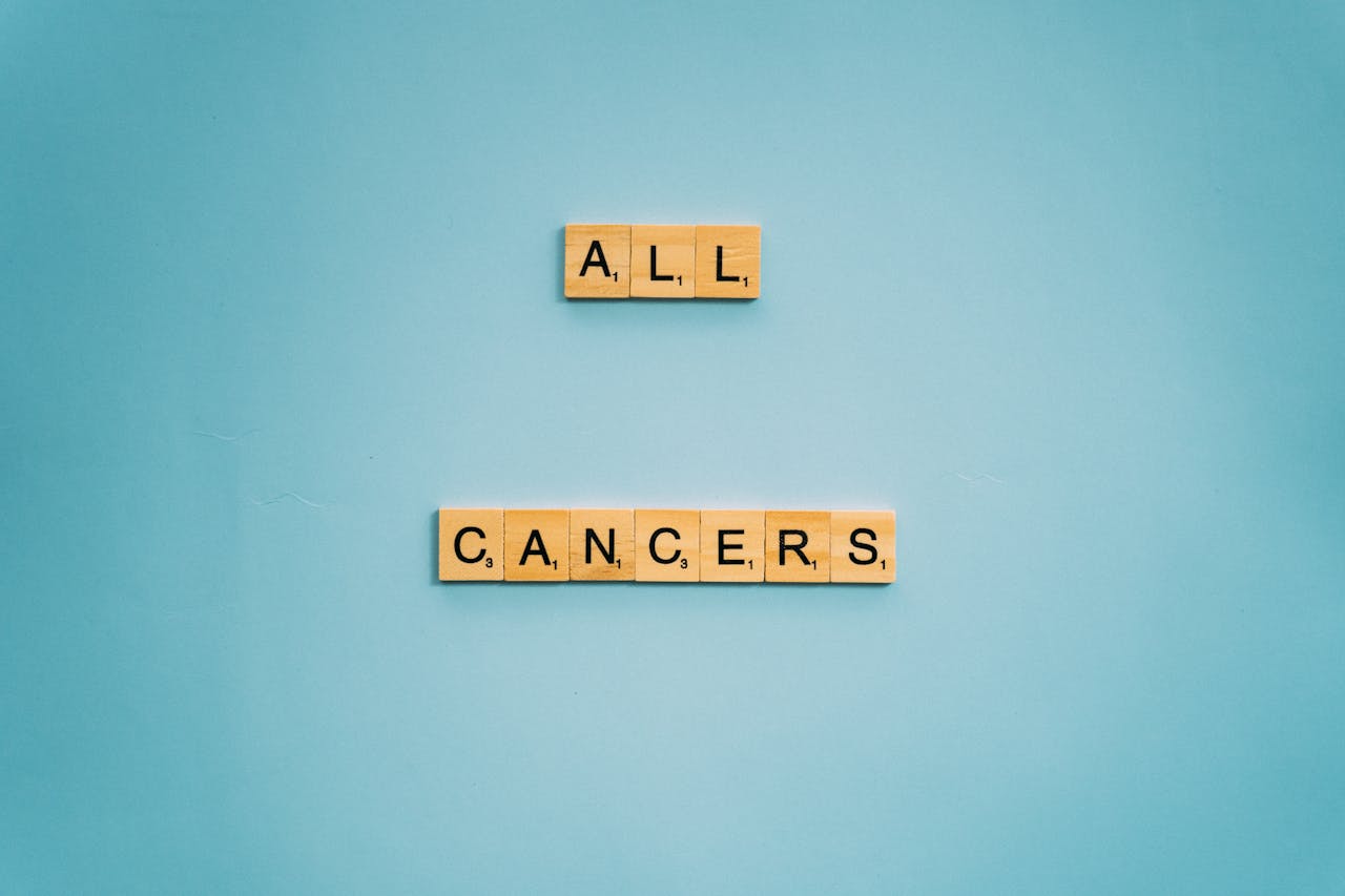 Home Scrabble tiles forming All Cancers on a light blue background, symbolizing cancer awareness.