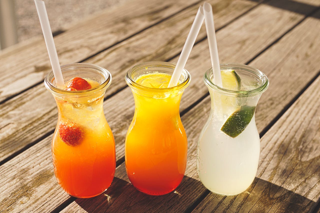 About Close-up of three refreshing beverages with citrus, strawberries, and lime on a sunny wooden table.